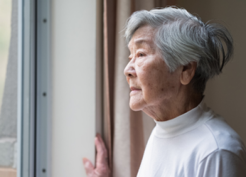 Older woman staring out of the window in despair
