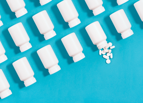 White pill bottles arranged in an organized fashion on a blue background with one bottle spilling pills