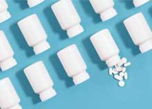 White pill bottles arranged in an organized fashion on a blue background with one bottle spilling pills