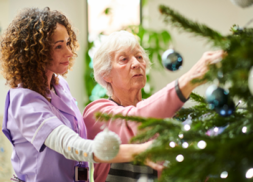 Younger woman helping older woman decorate Christmas tree.