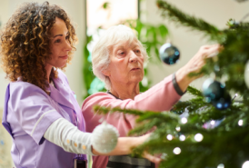 Younger woman helping older woman decorate Christmas tree.