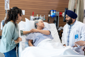 Older woman in hospital bed with two doctors at her bedside