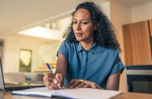 Woman writing notes while looking at laptop