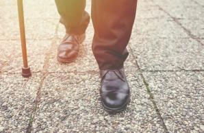 Man's feet and legs walking on sidewalk with assistance from a cane