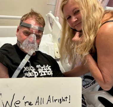 Ron McConnell in hospital bed holding a sign with Amy McConnell next to him