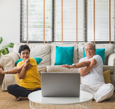 a couple doing stretches in front of a computer at home