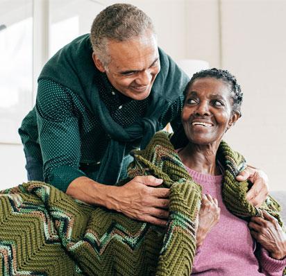 An older man takes care of his wife and wrapped a knit blanket around her shoulders