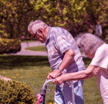 Older couple walking outside with assistance from walkers. Both of their backs are hunched over with stooped posture