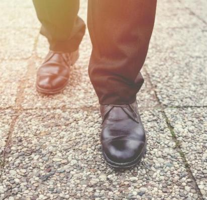 Man's feet and legs walking on sidewalk with assistance from a cane