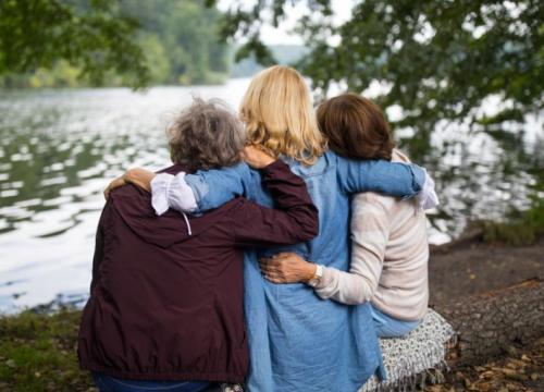 Three women sitting on a bench by a lake hugging