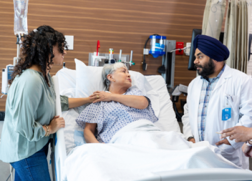 Older woman in hospital bed with two doctors at her bedside