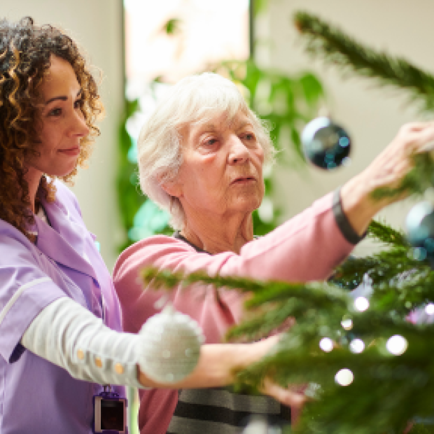 Younger woman helping older woman decorate Christmas tree.