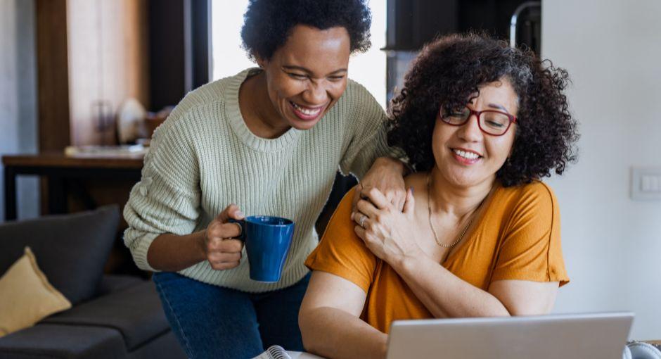 Two women holding hands, looking at a laptop