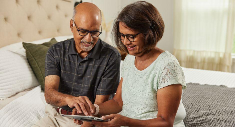 Husband and wife sitting on the bed looking at a tablet