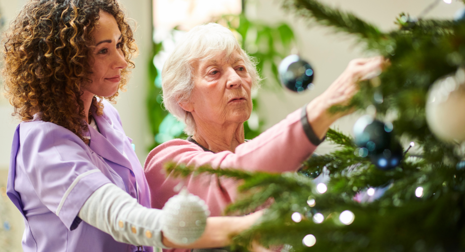 Younger woman helping older woman decorate Christmas tree.