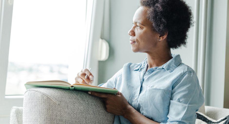 Woman looking out the window while writing in a notebook