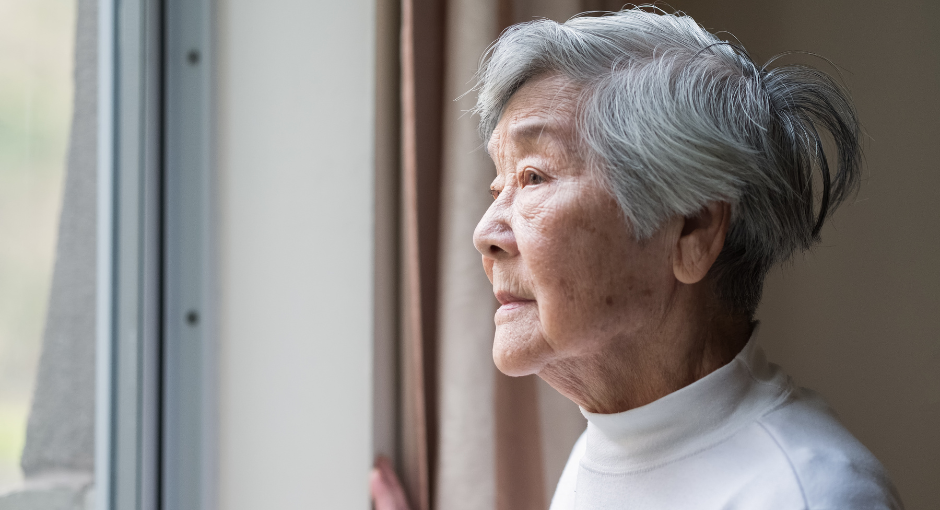 Older woman staring out of the window in despair
