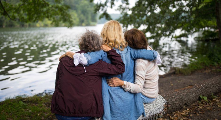 Three women sitting on a bench by a lake hugging