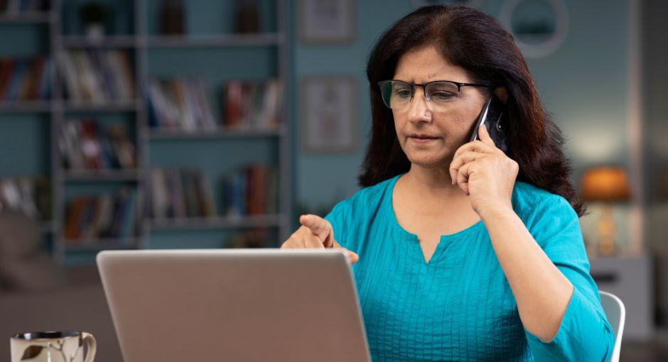 Woman on phone while pointing at laptop