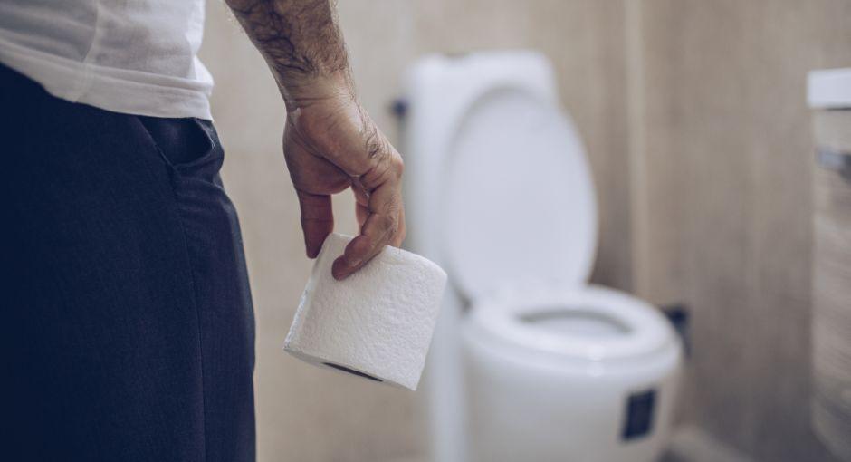 Man walking towards toilet holding toilet paper.