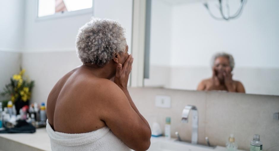 Woman in a bathroom looking at herself in the mirror and rubbing her face