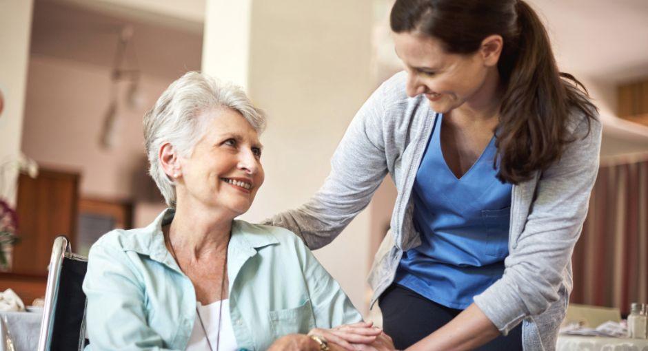 Nurse standing next to a lady in a wheelchair at nursing home