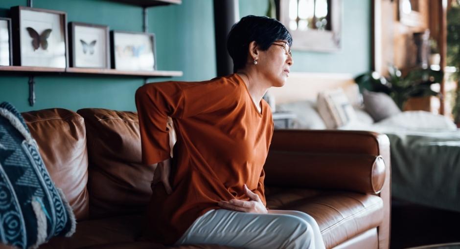 Woman sitting on couch holding her back in pain