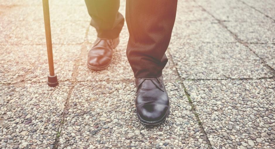 Man's feet and legs walking on sidewalk with assistance from a cane